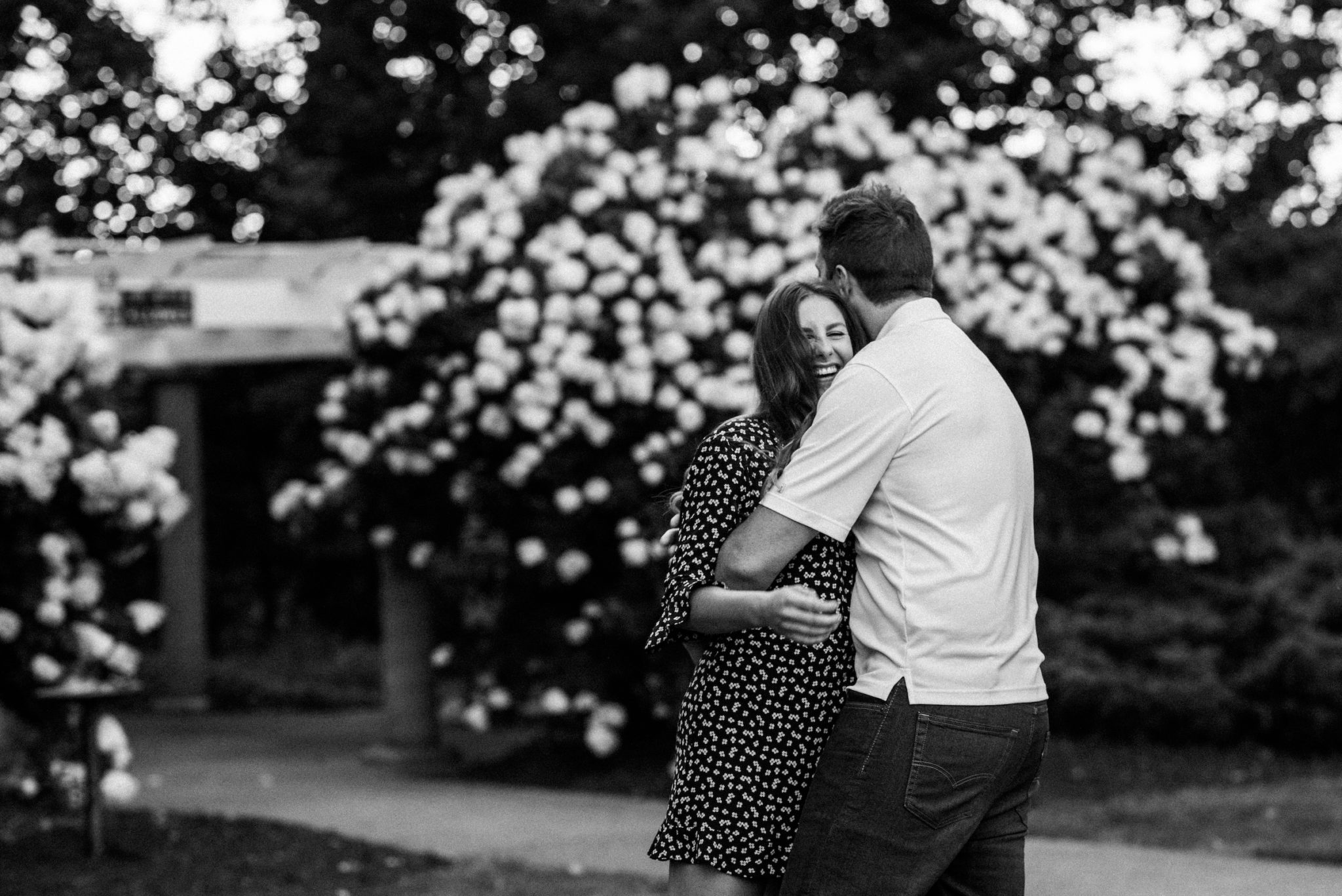 Black and white image of a couple laughing and hugging in a rose garden.