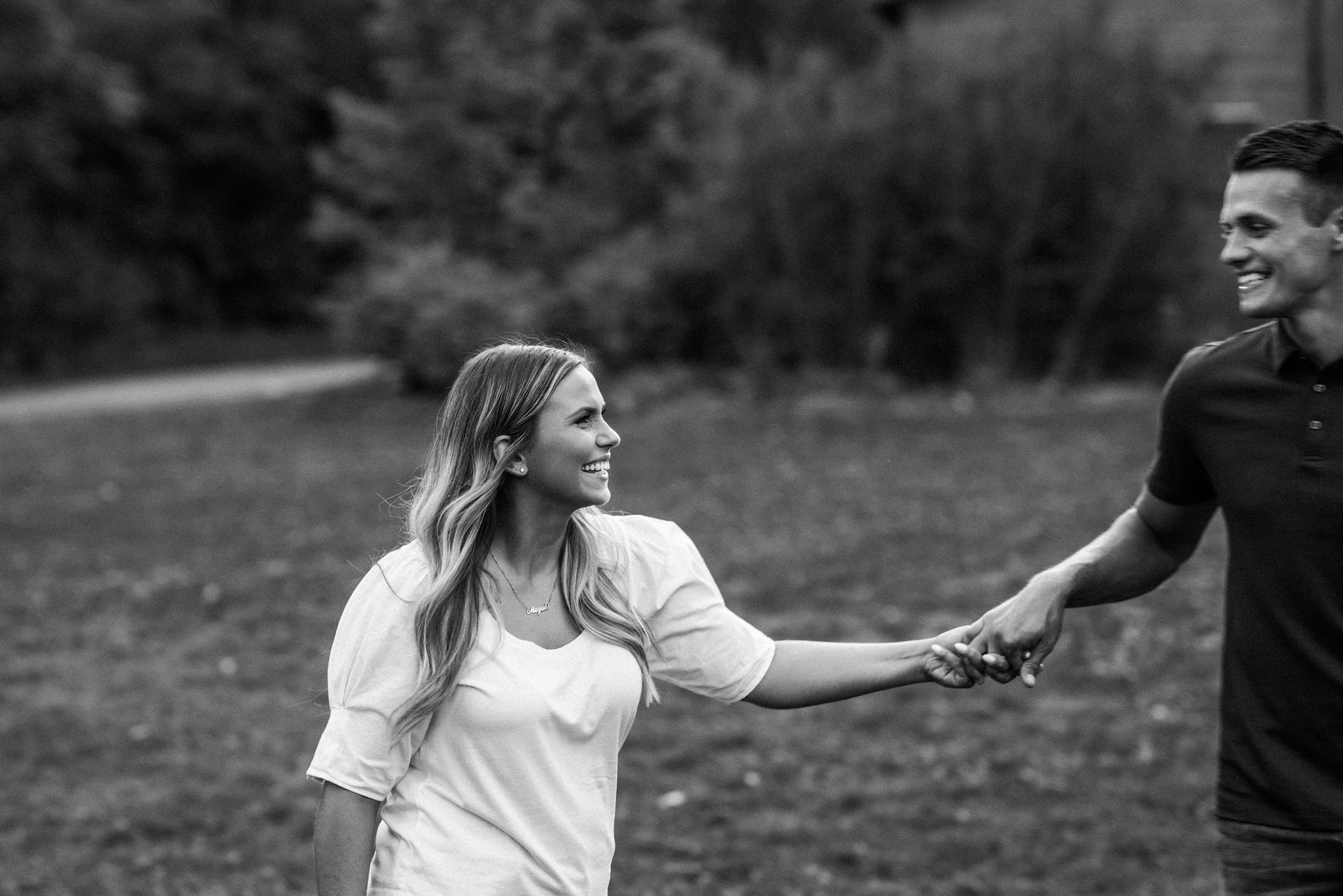 A black and white image of a couple holding hands and walking in grass.
