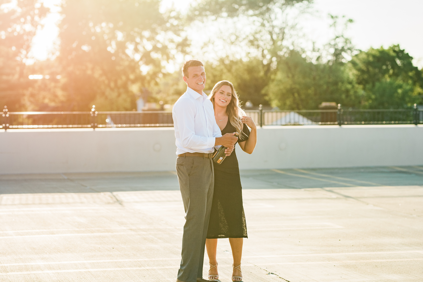 A portrait of a couple at sunset popping champagne on a rooftop.
