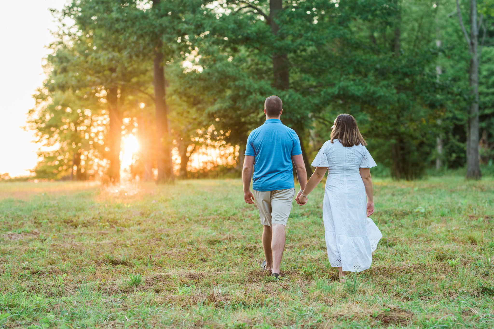 Couple walking in a field towards the sunset.
