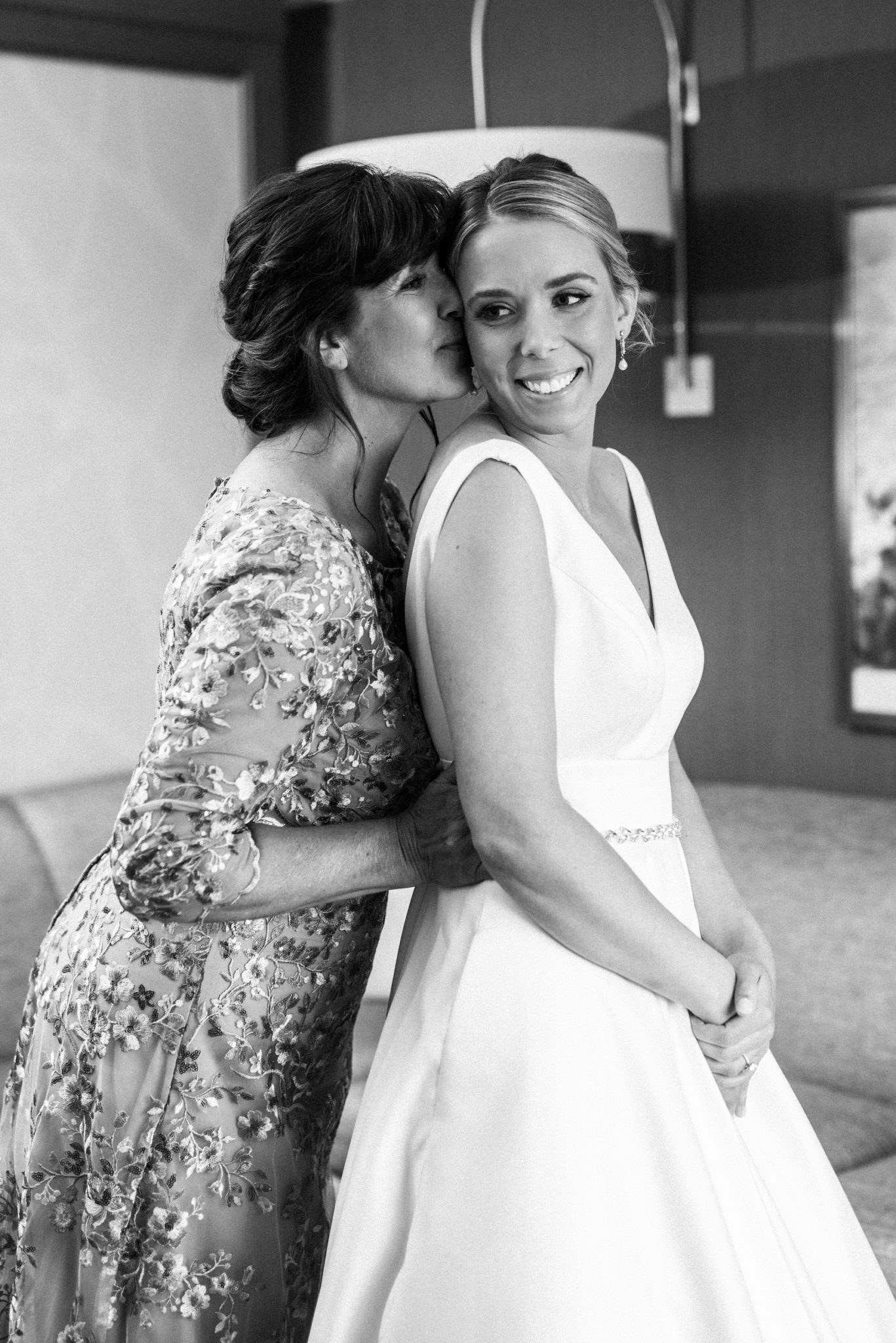 a mom kissing her daughter while getting her dressed in her wedding dress