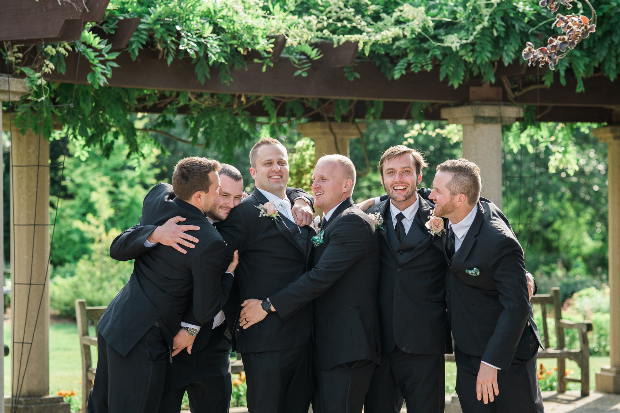 groomsmen hugging the groom during wedding pictures on campus in east lansing michigan