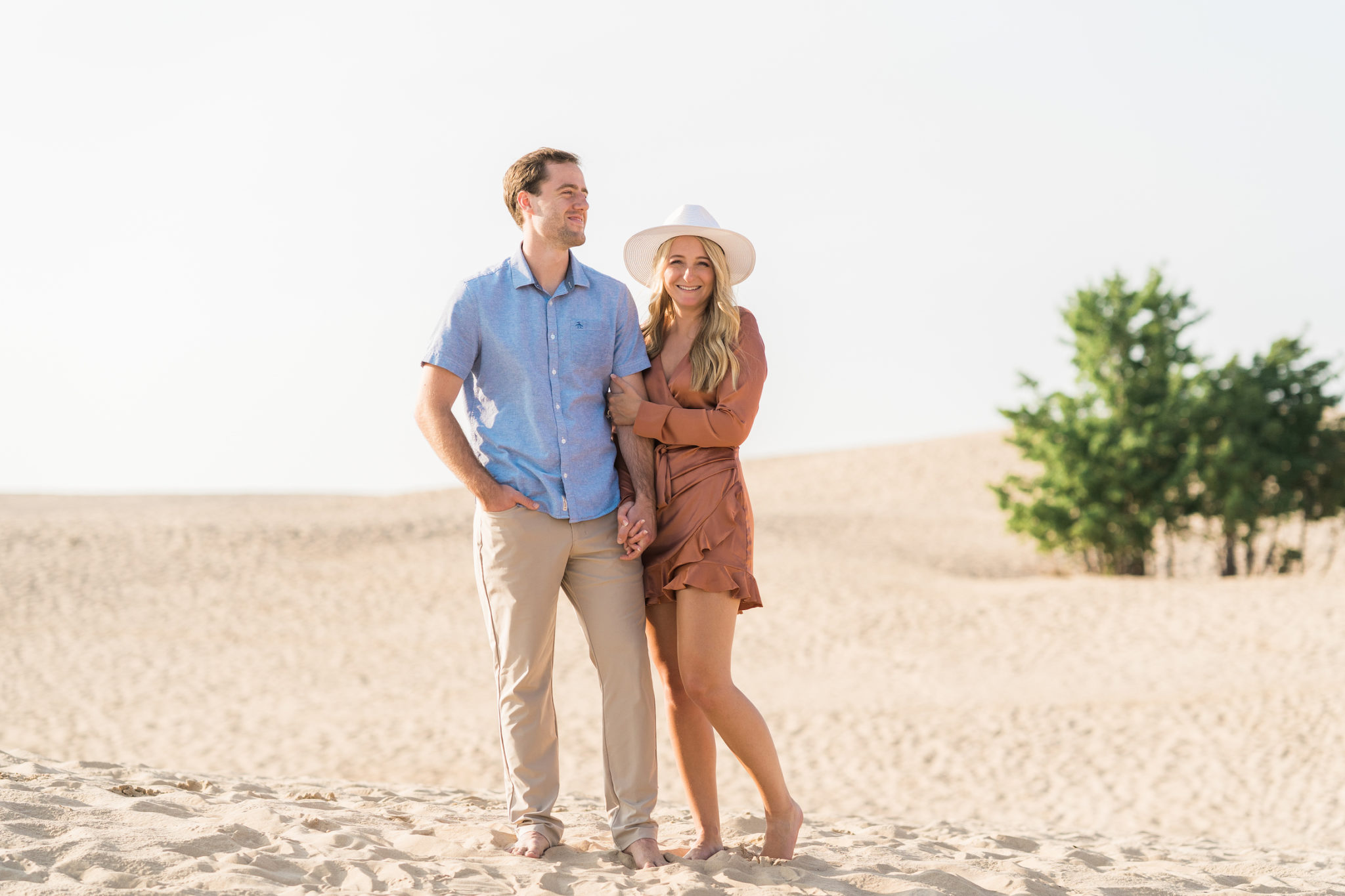 a couple holding hands during their engagement photo session at the silver lake sand dunes in michigan