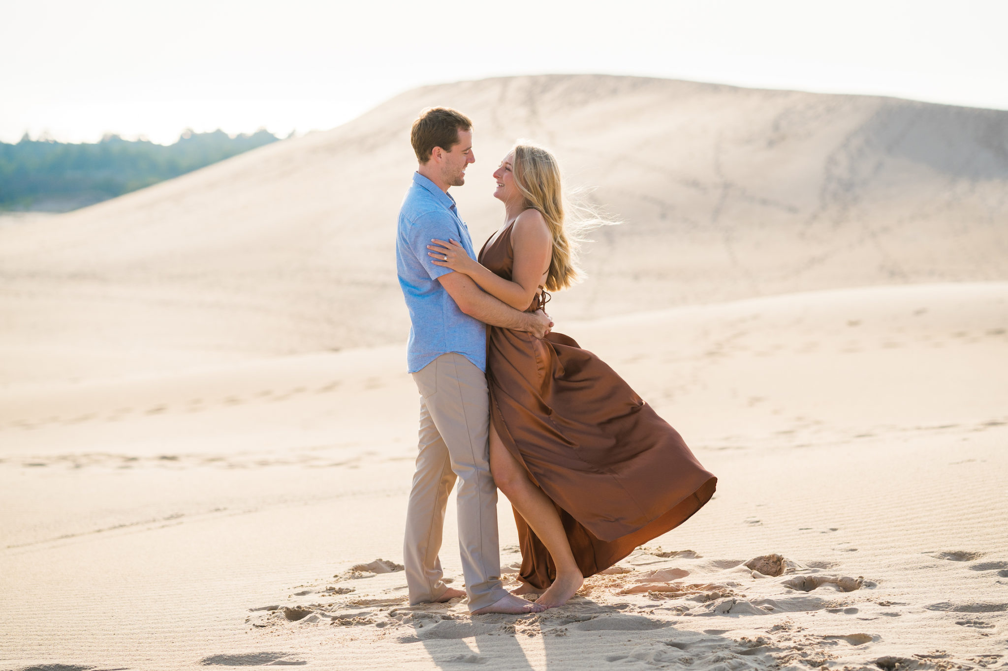 a couple looking at one another and smiling during their engagement session at silver lake sand dunes in michigan