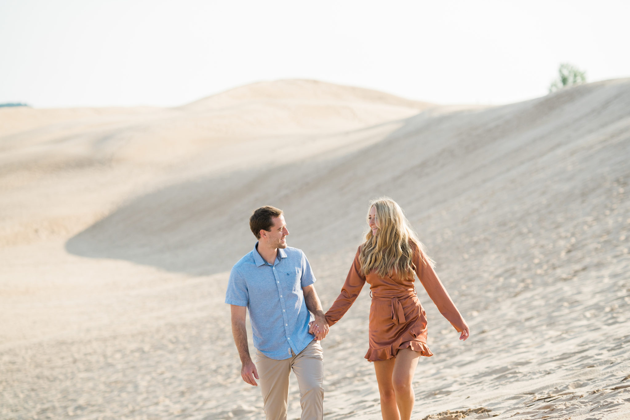 a couple walking on the michigan sand dunes during their summer engagement photos