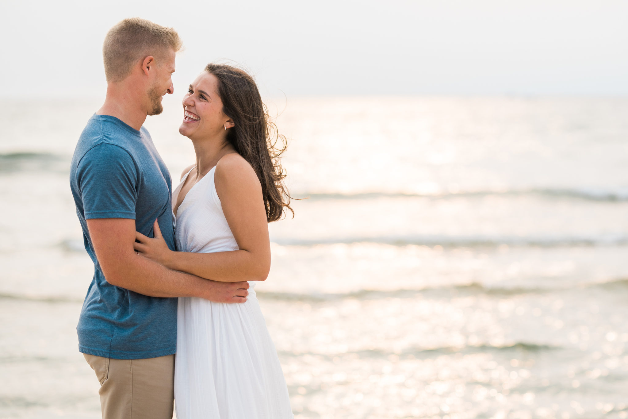 a couple embracing and smiling during their sunset grand haven beach engagement session
