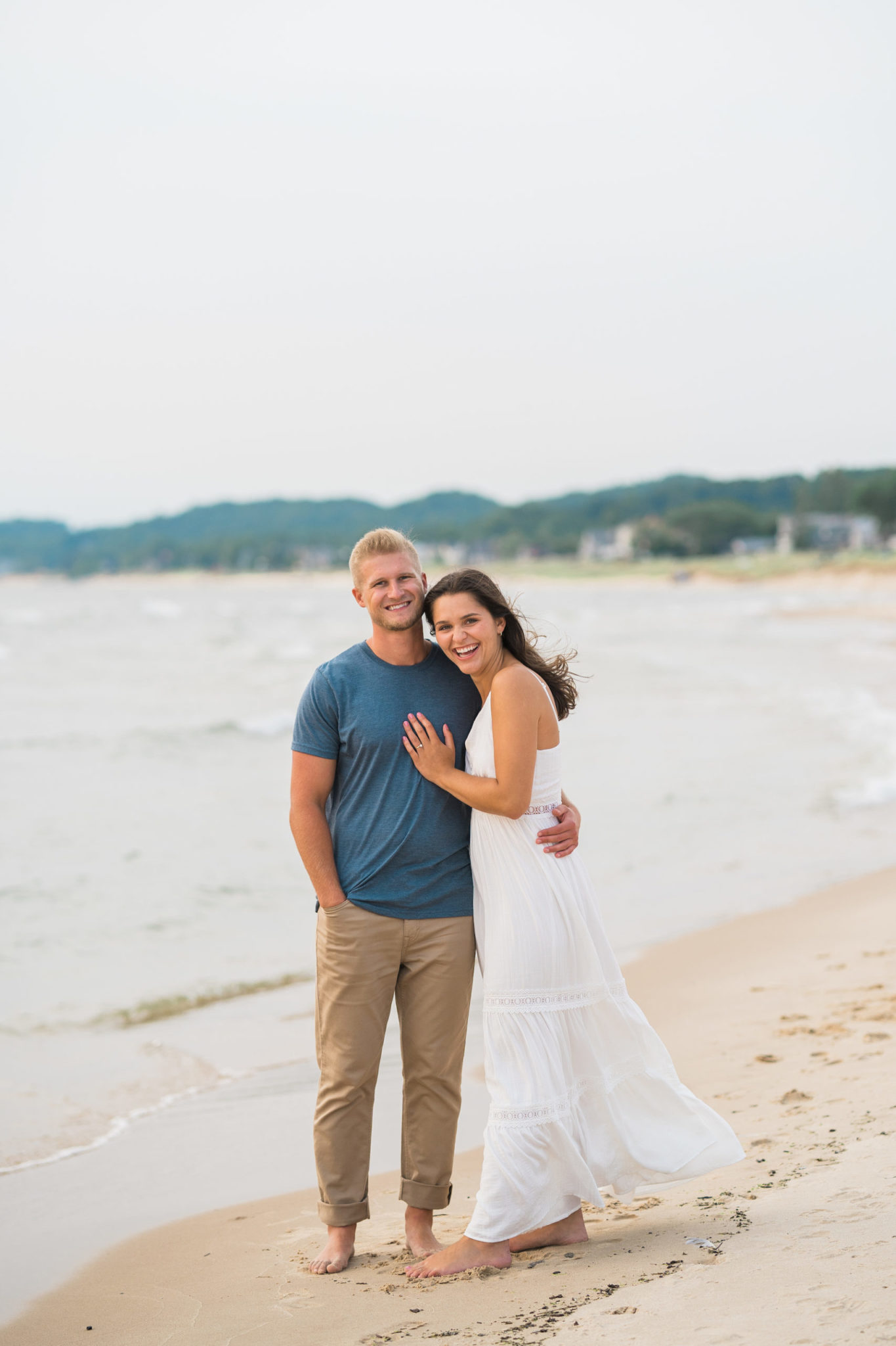 a couple embracing and smiling during their sunset grand haven beach engagement session